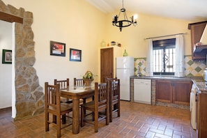 A dining area with a wooden table and chairs, a stone wall, a refrigerator, a sink, and a window with curtains. - House with Paddle Court 'Casa Roche Noble 2' with Private Pool, Private Terrace and Wi-Fi (Conil de la Frontera)