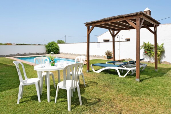 A poolside area with a pergola, lounge chairs, and a table with chairs.