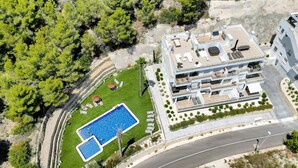An aerial view of a modern multi-story building with a rooftop pool, a landscaped garden, and a curved road nearby. - Apartment 'Real De Ifach - Atico' with Sea View, Wi-Fi and Air Conditioning (Calpe)