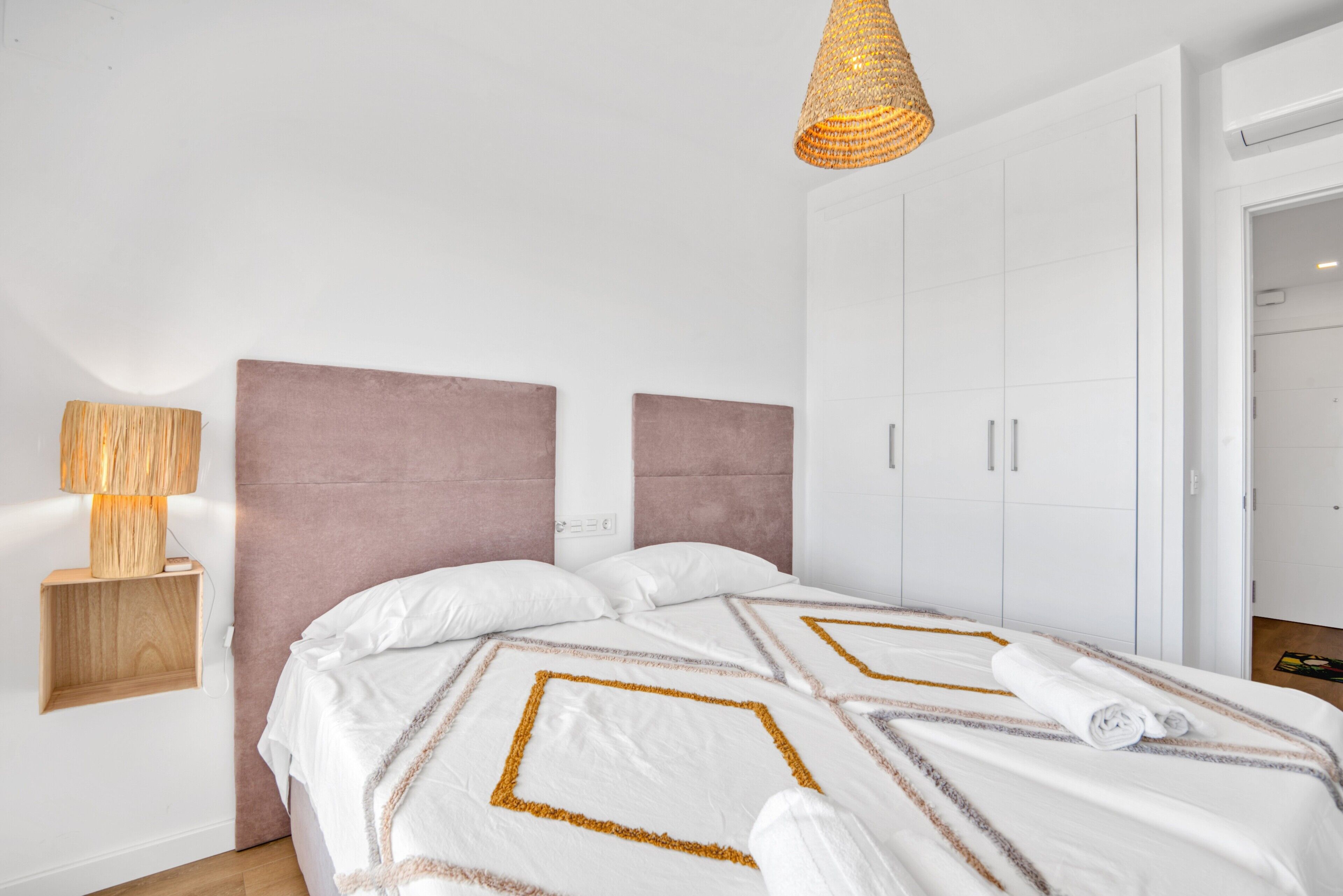 A bedroom with a bed, a bedside lamp, a wardrobe, and a hanging light fixture.