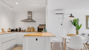 A modern kitchen with white cabinetry, a central island, a stainless steel range hood, and a dining area with white chairs and a table. - Apartment 'Real De Ifach - Atico' with Sea View, Wi-Fi and Air Conditioning (Calpe)