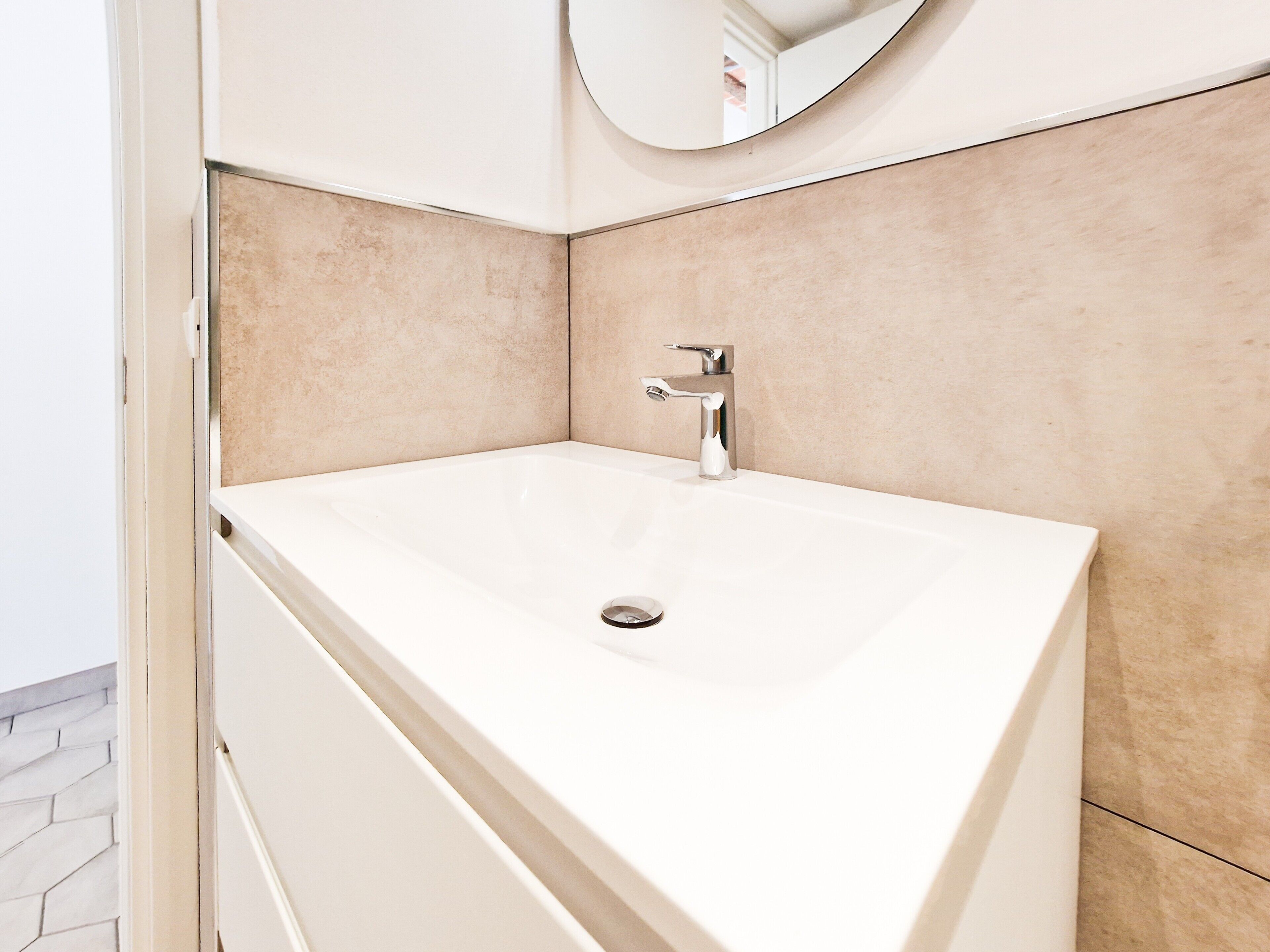 Un bagno con un lavandino bianco, uno specchio e pareti rivestite di piastrelle beige.