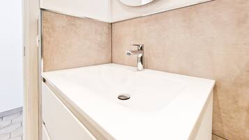 Un bagno con un lavandino bianco, uno specchio e pareti rivestite di piastrelle beige.