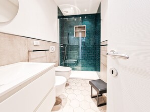 A modern bathroom with a white bathtub, a toilet, a shower with a glass door, and a hexagonal tile floor.