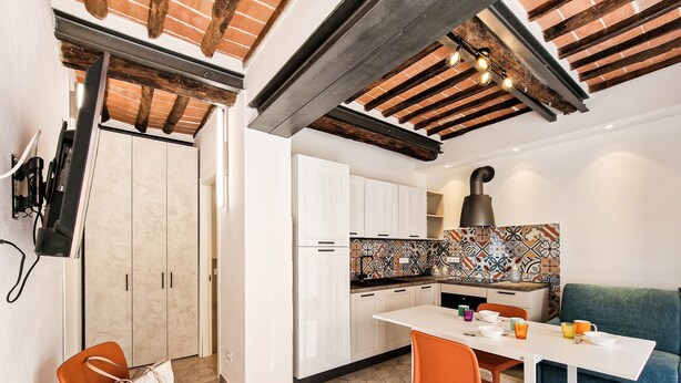A compact kitchen with a dining area, featuring a hexagonal tile floor, white cabinetry, and a wooden ceiling.