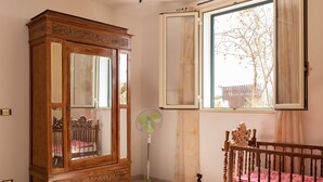 Un dormitorio con un armario de madera, una cama con cubrecama rosa, un ventilador de pie y una ventana con cortinas.