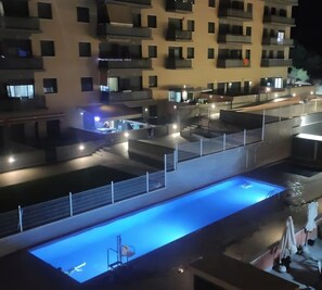 A multi-level residential building with balconies, a swimming pool, and outdoor seating areas.