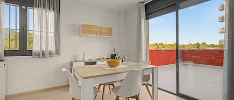 A modern dining area with a wooden table and chairs, a large window with curtains, and a view of the outdoors.