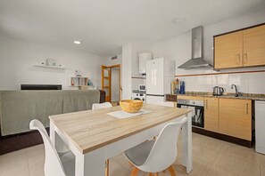 A modern kitchen with a wooden table, white chairs, and a built-in oven.