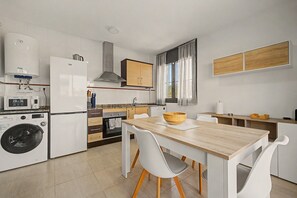 A modern kitchen with a wooden dining table, white chairs, a built-in oven, and a washing machine.