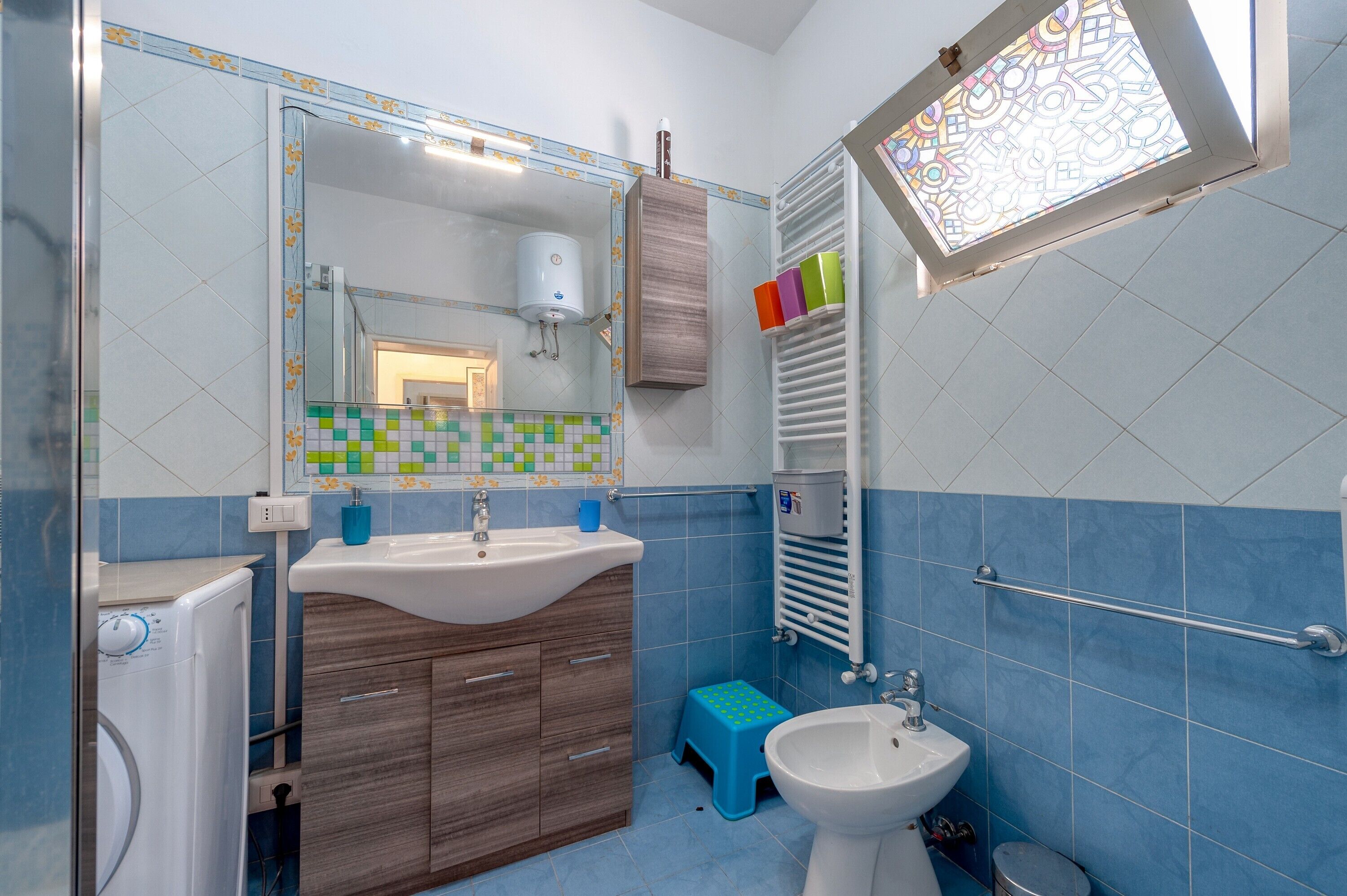 Een badkamer met een wastafel, spiegel, toilet en een klein opstapkrukje.