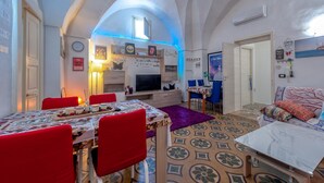 Un comedor con una mesa dispuesta para dos, un televisor y una zona de estar acogedora con un sofá y una alfombra estampada.