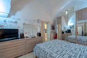 Une chambre à coucher avec un lit, une commode, une télévision et un miroir.