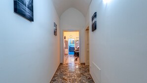 Un pasillo con baldosas estampadas, una puerta que da a una habitación con una silla y una mesa azules, y cuadros colgados en la pared.