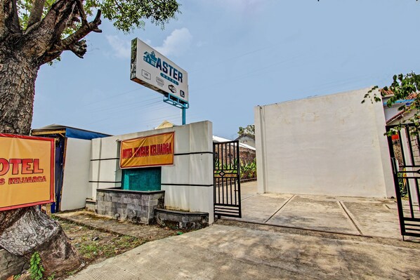 L’entrée d’un hôtel, avec un panneau indicateur, une grille et un arbre.
