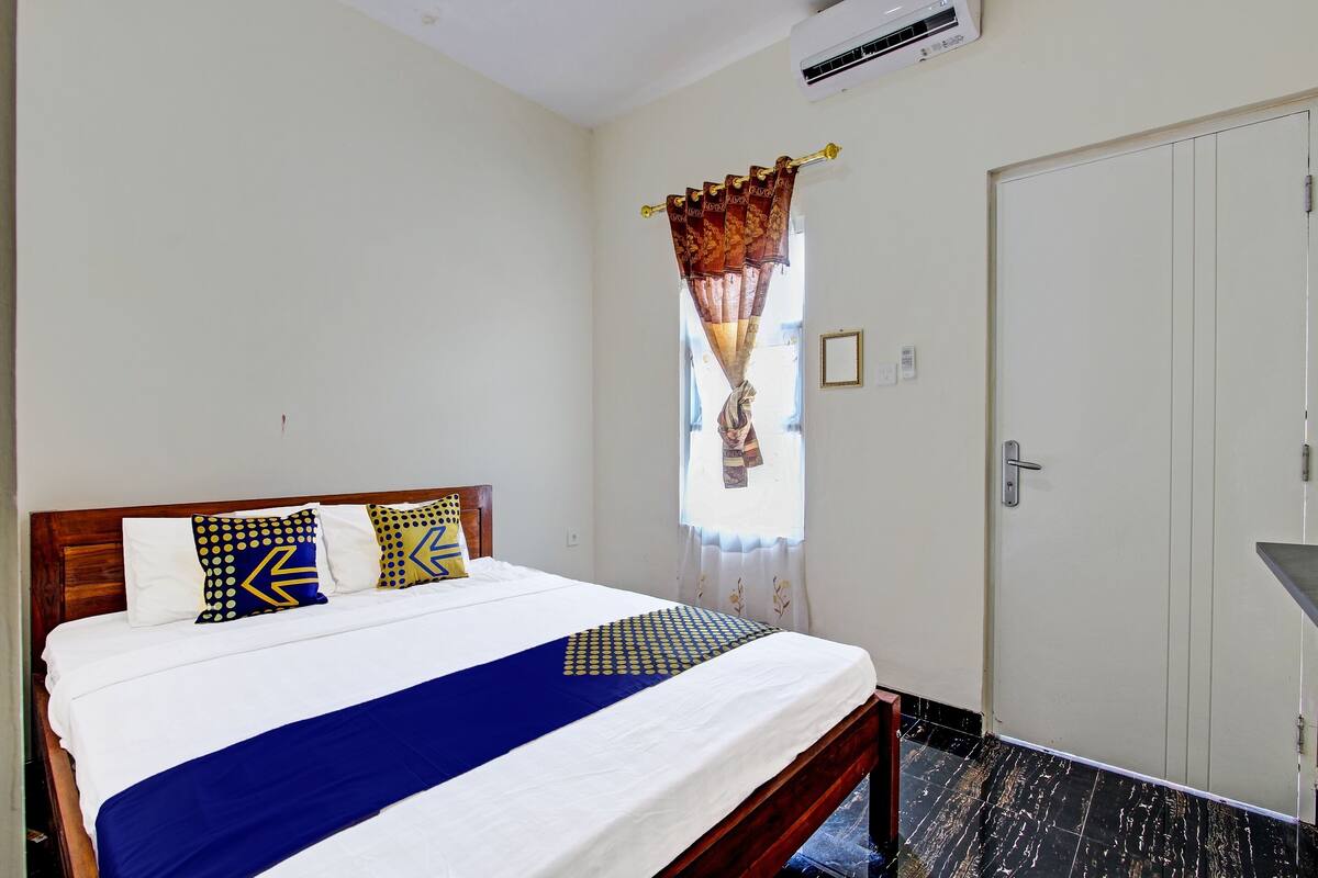 A hotel room with a bed, a window with curtains, a door, and an air conditioning unit.