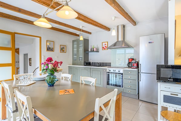 Una cocina moderna con vigas de madera, electrodomésticos de acero inoxidable y un comedor con sillas blancas y un jarrón de flores.