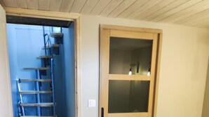 Une chambre à coucher comprenant un lit, une commode en bois, une armoire à portes vitrées et un escalier menant à une autre pièce.