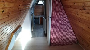 Un étroit couloir en bois, orné d’un rideau à carreaux, avec une porte et une vue sur une pièce dotée d’une fenêtre.