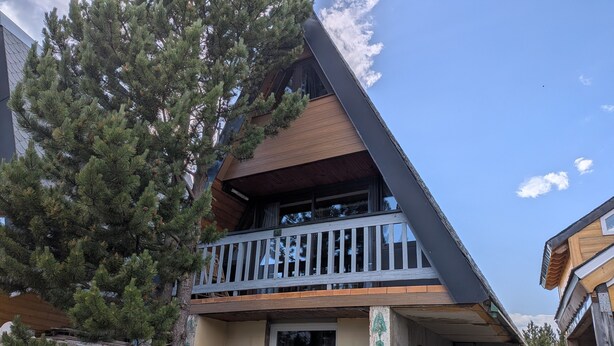 Un immeuble à plusieurs étages doté d’un balcon, entouré d’arbres et d’un terrain rocheux.