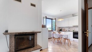 Une cuisine avec des meubles blancs, une table à manger avec des chaises, un four encastré et une fenêtre avec des stores.