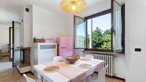 Un coin repas comprenant une table, des chaises, un panier, un appareil électroménager rose et une fenêtre avec des rideaux.