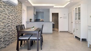 Een moderne keuken met een inbouw eiland, in het plafond geïntegreerde verlichting, en een eethoek met een donker houten tafel en stoelen.