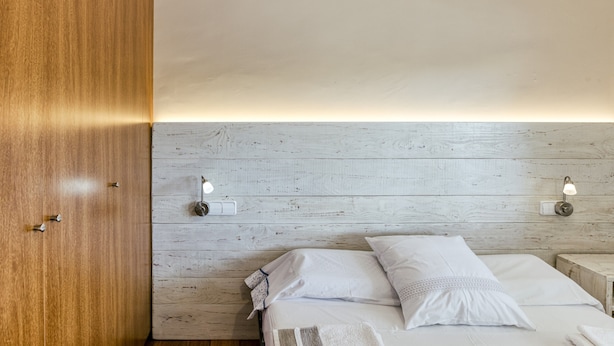 A room with a wooden wardrobe, a bed with white bedding, and two wall-mounted light fixtures. - Apartment "Olga" with Private Terrace and Wi-Fi (Platja d'Aro)
