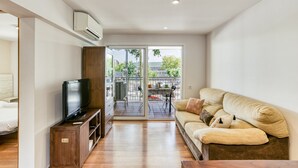 A modern living room with a flat-screen TV on a wooden stand, a beige sofa with cushions, and a sliding glass door leading to an outdoor patio with a table and chairs. - Apartment "Olga" with Private Terrace and Wi-Fi (Platja d'Aro)