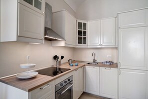 A kitchen with white cabinets, a stainless steel range hood, a double sink, and a wooden countertop.