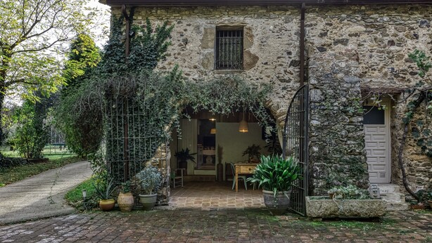 Un bâtiment en pierre doté d’une entrée rustique, de plantes en pot et d’un chemin pavé en briques.