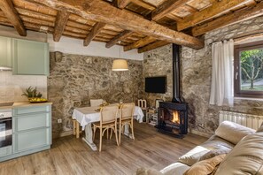 Un intérieur rustique avec un mur en pierre, des poutres en bois au plafond, un coin repas, une cheminée et un canapé.
