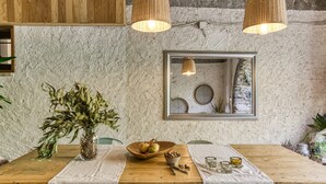 Un coin repas rustique avec une table en bois, une nappe blanche et un vase rempli de feuilles vertes.