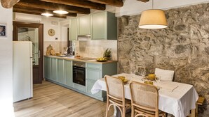 Une cuisine avec un mur en pierre, des poutres en bois et un coin repas avec une table mise pour deux personnes.