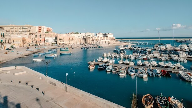 A marina with numerous boats docked, a waterfront promenade, and buildings with balconies overlooking the water.