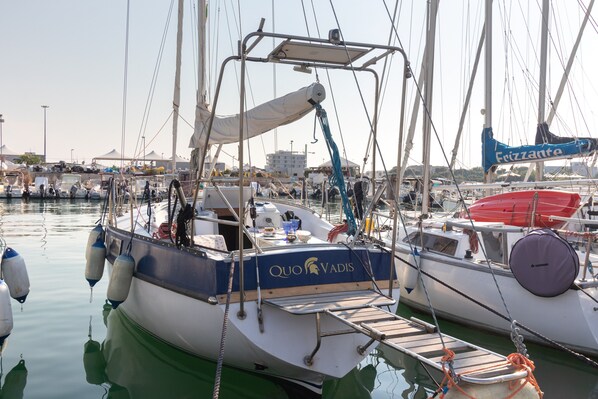 Un port de plaisance où sont amarrés plusieurs bateaux, dont un sur lequel on peut voir les inscriptions « QUOVADIS » et « Fezzantra ».