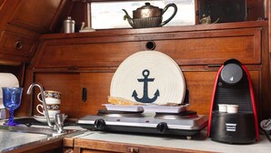 A kitchenette with a tea pot, a coffee maker, a plate with an anchor design, and a cup.