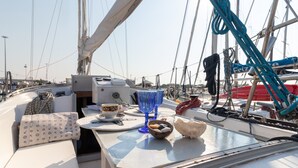A boat deck with a table, cushions, a bowl, and a blue glass.