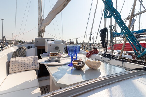 Un pont de bateau avec une table, des coussins, un bol et un verre bleu.