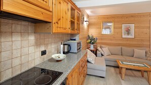 A kitchen with wooden cabinets, a microwave, a toaster, and a stove. There is a beige sofa and a small table with a placemat. - Holiday Apartment 'Casa Silvia' with Mountain View, Terrace & Wi-Fi (Livigno)