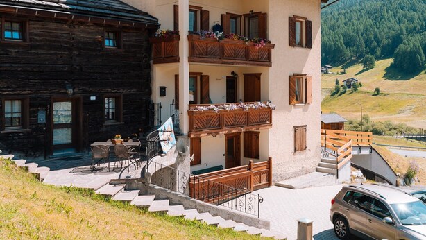 A two-story building with wooden balconies, a stone staircase, and a car parked in front. - Holiday Apartment 'Casa Silvia' with Mountain View, Terrace & Wi-Fi (Livigno)