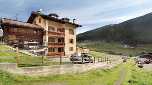 A two-story building with a wooden facade and a balcony, situated in a hilly area with a clear sky. - Holiday Apartment 'Casa Silvia' with Mountain View, Terrace & Wi-Fi (Livigno)