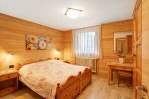 Een houten kamer met een bed, een bureau, een stoel, een radiator en een schilderij aan de muur.