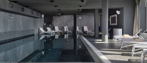 A modern indoor pool area with multiple lounge chairs and a clear pool.