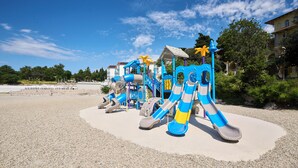 Un parque infantil con toboganes y estructuras para escalar, rodeado de grava y árboles.