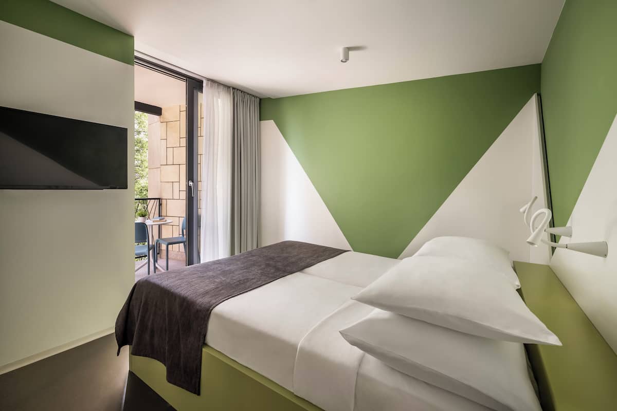 A hotel room with a bed, a TV mounted on the wall, and a view of the outside balcony.
