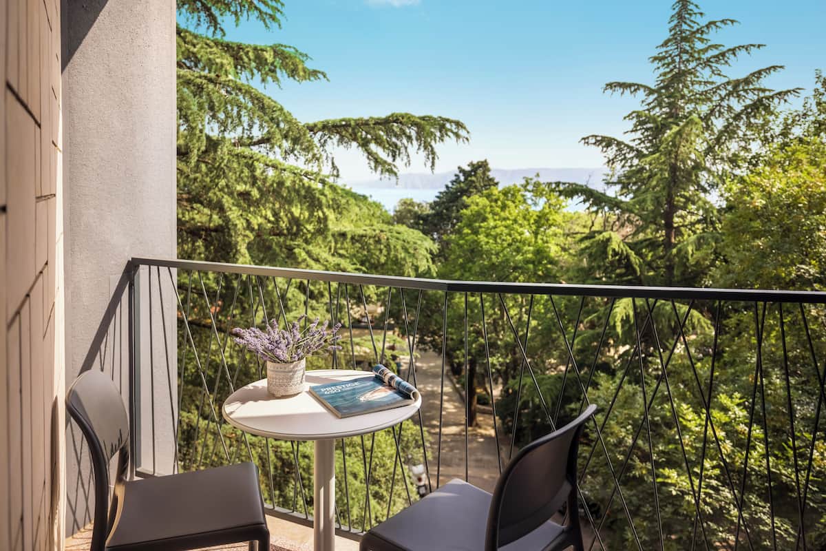 A balcony with two chairs, a small table with a book and a potted plant, and a view of a forested area.