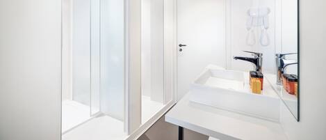 A modern bathroom with a glass shower enclosure, a white sink with a mirror, and a towel rack.