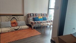 Uma sala de estar com dois sofás, um com capa estampada e outro com padrão geométrico. Há uma mesinha redonda com um controle remoto sobre ela.