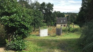 Paesaggio rurale con un edificio in pietra, un albero grande e un prato erboso.